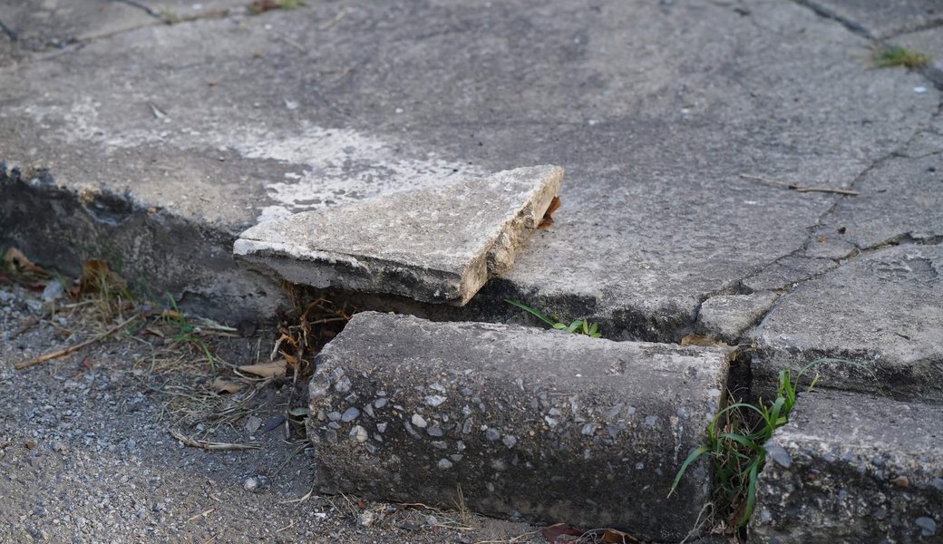 Cracked and uneven sidewalk slab with a raised edge forming a trip hazard